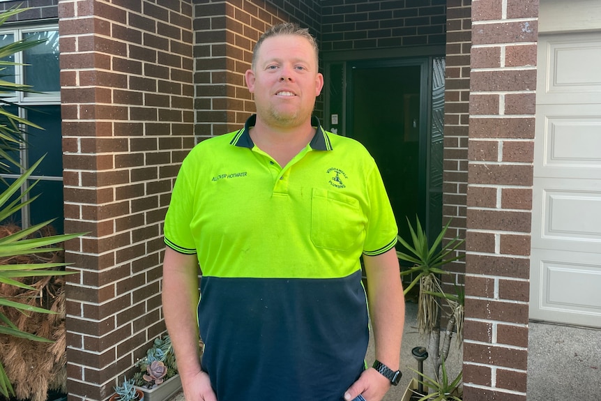 A man wearing a high-vis yellow shirt stands outside a house.