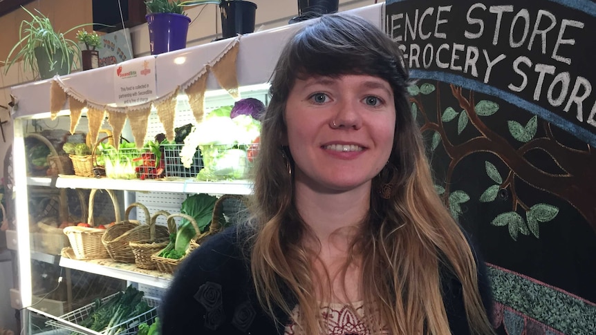 Astrid Ryan standing inside the store in front of shelves with baskets of vegetables.