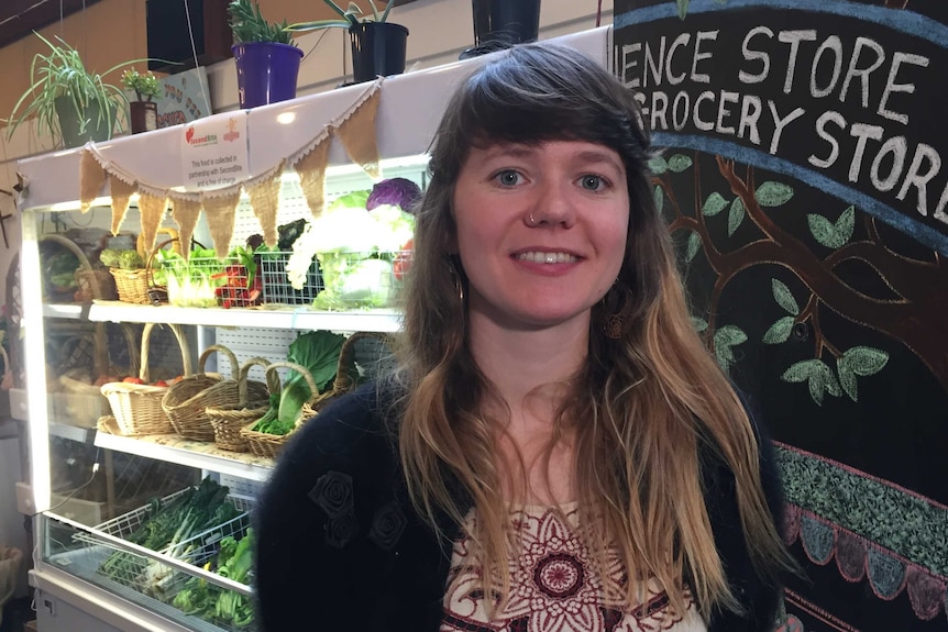 Astrid Ryan standing inside the store in front of shelves with baskets of vegetables.