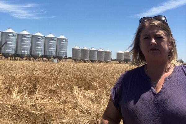 Woman in purple top and sunglasses on head. Hay in background with machinery.