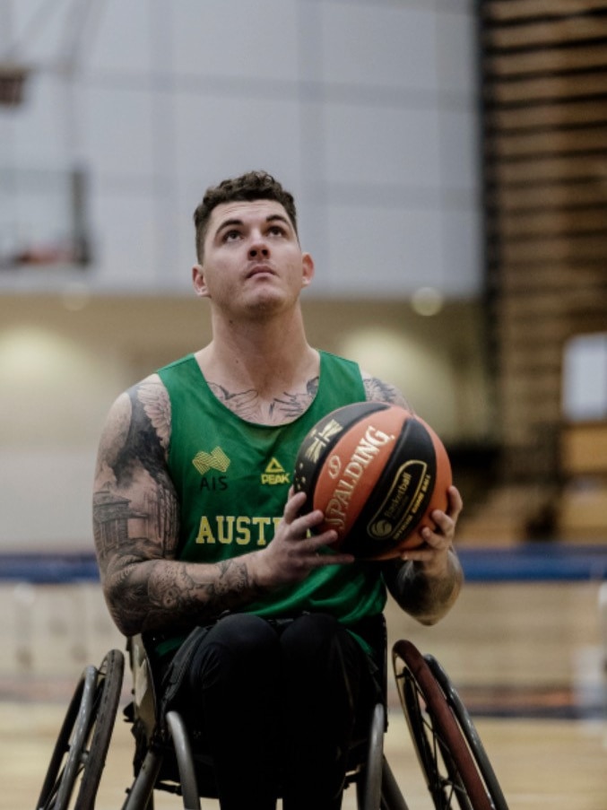 A man in a wheelchair wearing a green basketball top with a basketball in hand