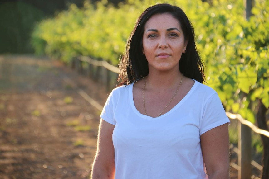 A woman stands in front of a row of crops.