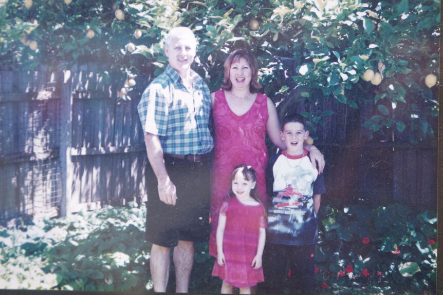 A family of four standing in front of a garden and fence.