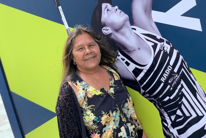 A woman stands in front of a poster of Ash Barty about to serve.