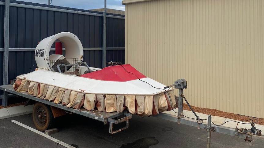 A hovercraft sits on a trailer in a car park. 