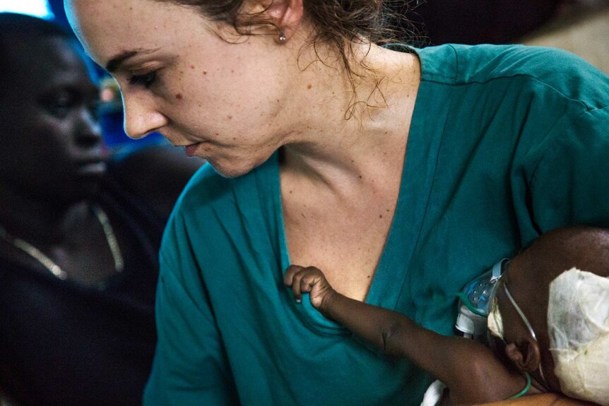 Baby Nyanene latches on to the green shirt of nurse Jessica Hazelwood