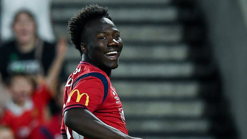 Nestory Irankunda celebrates a goal for Adelaide, smiling and looking back over his shoulder.