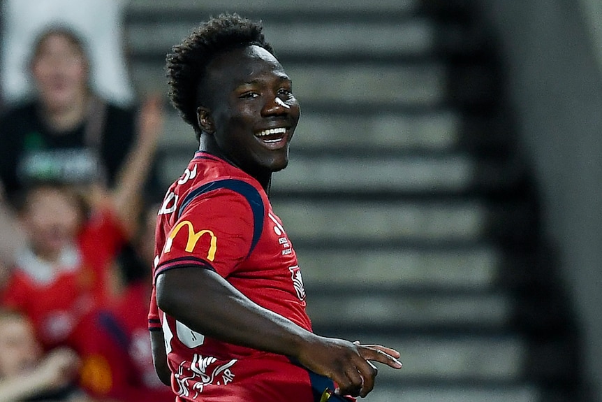 Nestory Irankunda celebrates a goal for Adelaide, smiling and looking back over his shoulder.