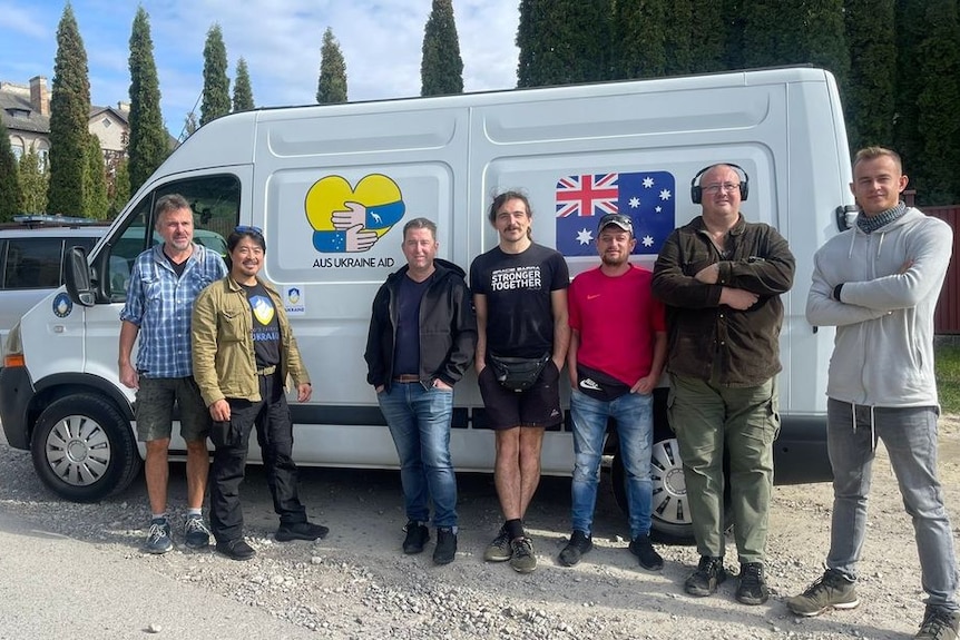 A group of people standing in front of a white van with the Australian flag on it.