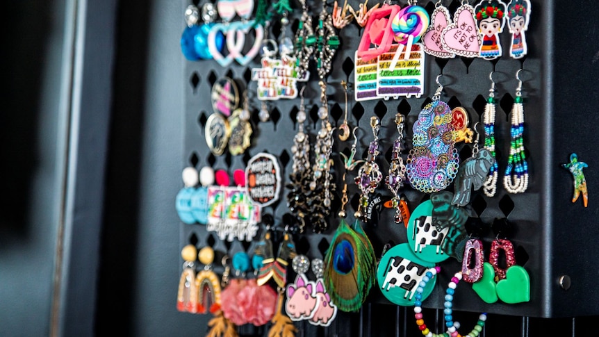 About 25 pairs of fun, colourful, dangly earrings hang from a black board.