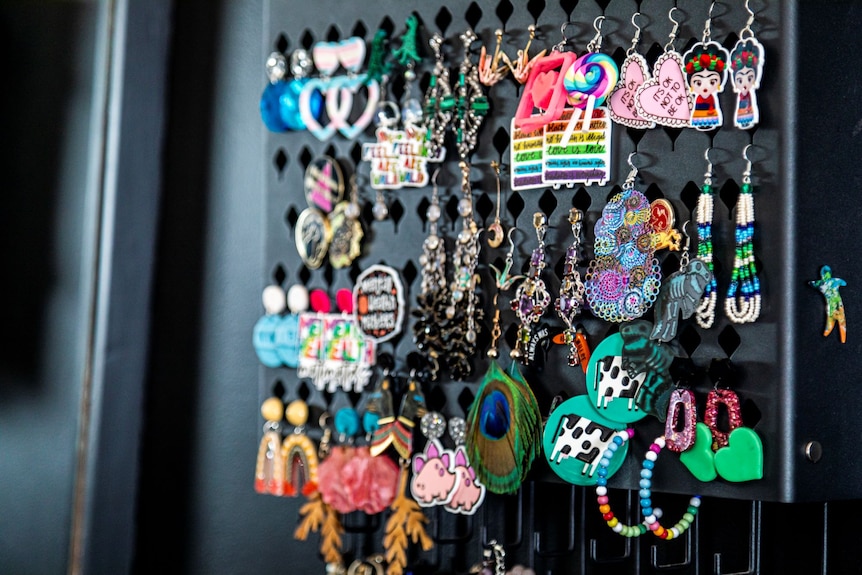 About 25 pairs of fun, colourful, dangly earrings hang from a black board.