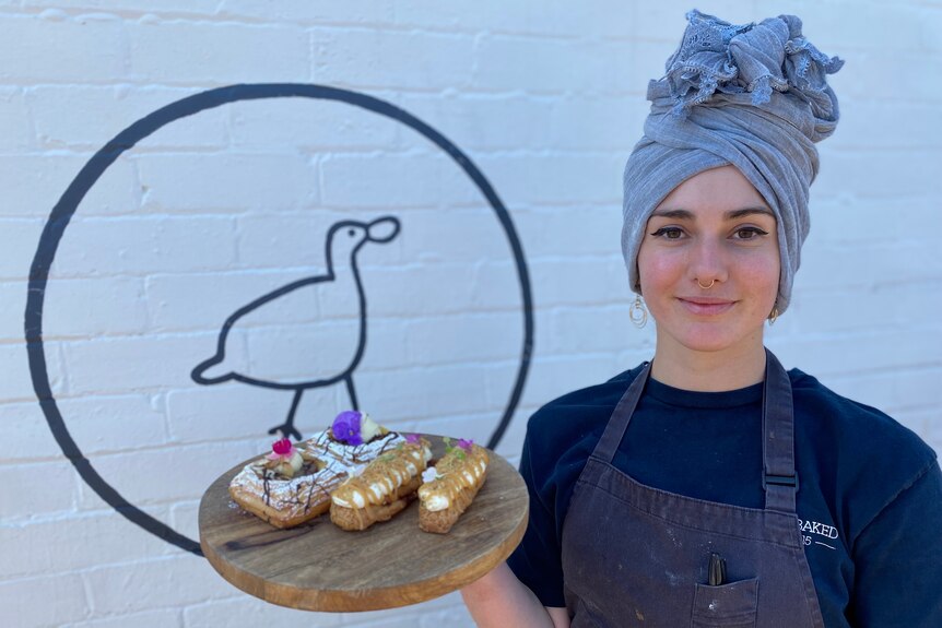 Female with head wrap holds platter full of pastries with edible flowers on them 