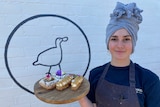 Female with head wrap holds platter full of pastries with edible flowers on them 