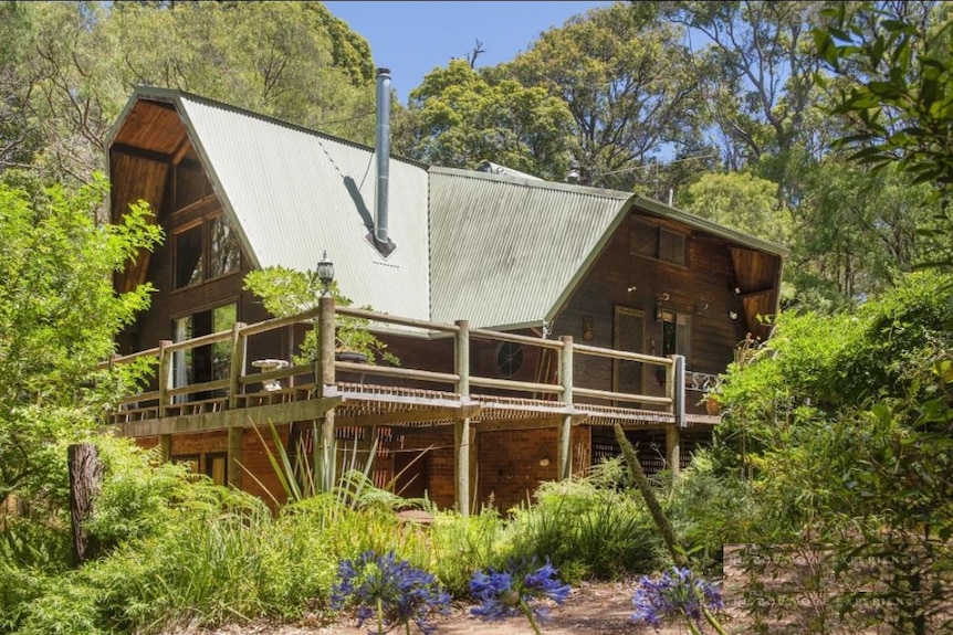 Garden surrounds a two-storey cabin-style home with a dark green metal roof.