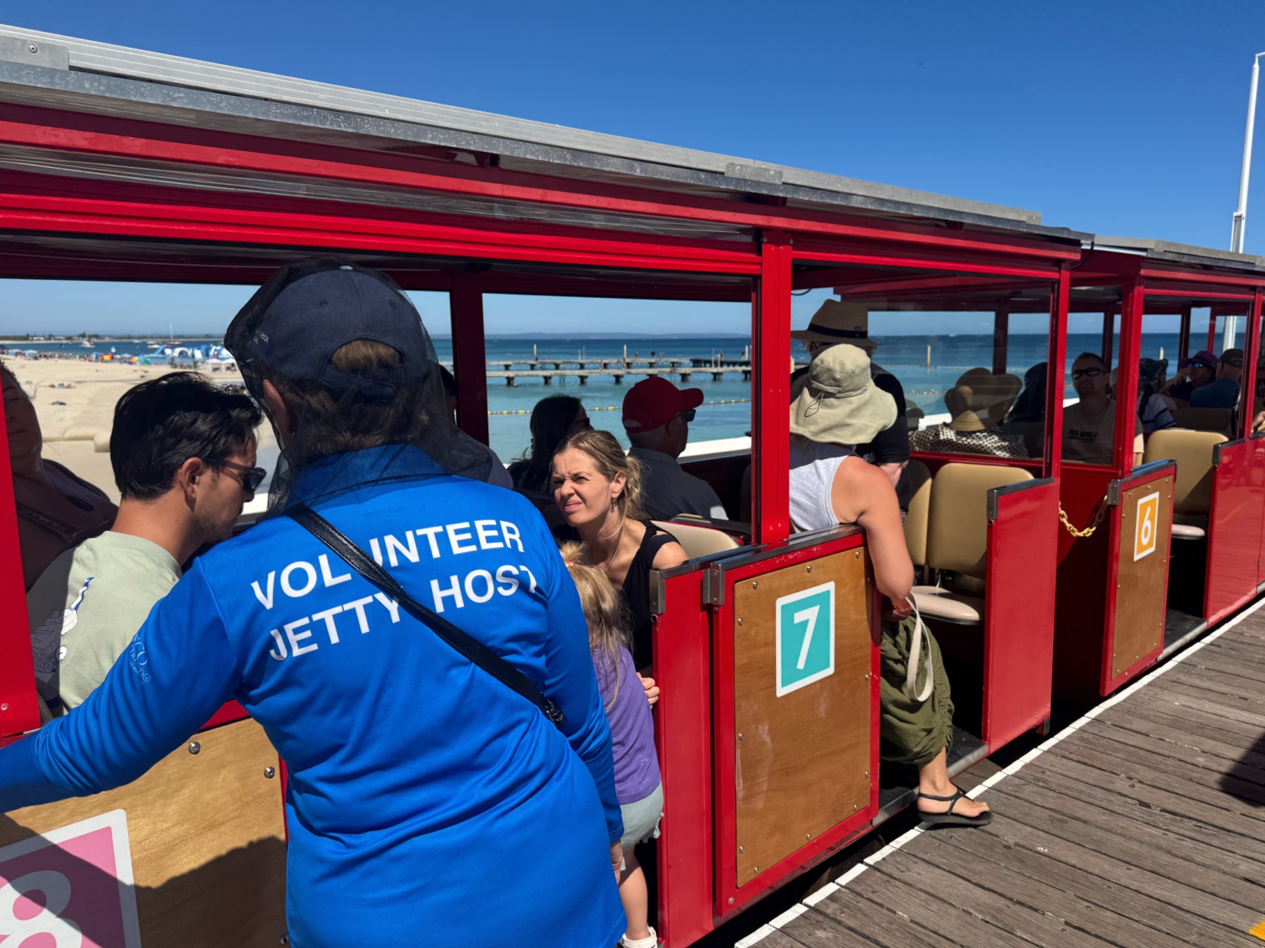 Um voluntário ajuda as pessoas a sentarem-se no trem Busselton Jetty
