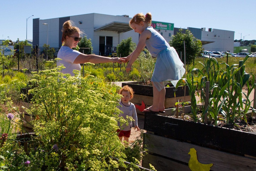 A mother and two children play among garden beds.