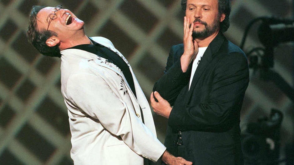 Robin Williams shares a laugh with Billy Crystal on stage at Comic Relief in 1998.
