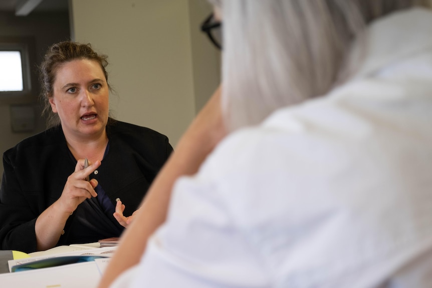 Kate speaks to two women at a low table.