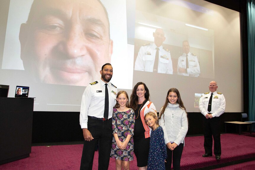 Lieutenant Commander Samuel Sheppard stands with his family during a virtual presentation ceremony.