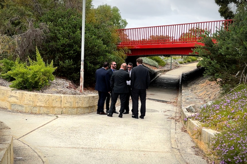 A group of men in black suits huddle in a footpath underpath