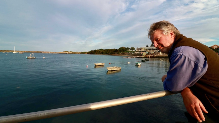 Alan Nicholls pictured looking over the pier at Apollo Bay with the Apollo Bay Fisherman's Coop in the background.