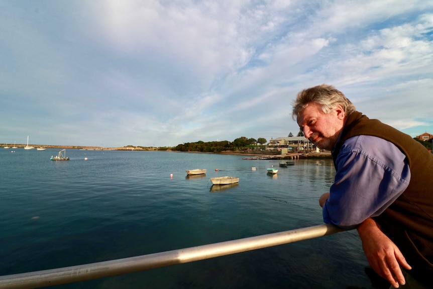 Alan Nicholls pictured looking over the pier at Apollo Bay with the Apollo Bay Fisherman's Coop in the background