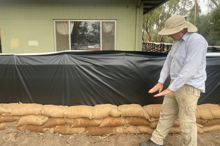 A man pointing down to a fence surrounding his home with sandbags nearby