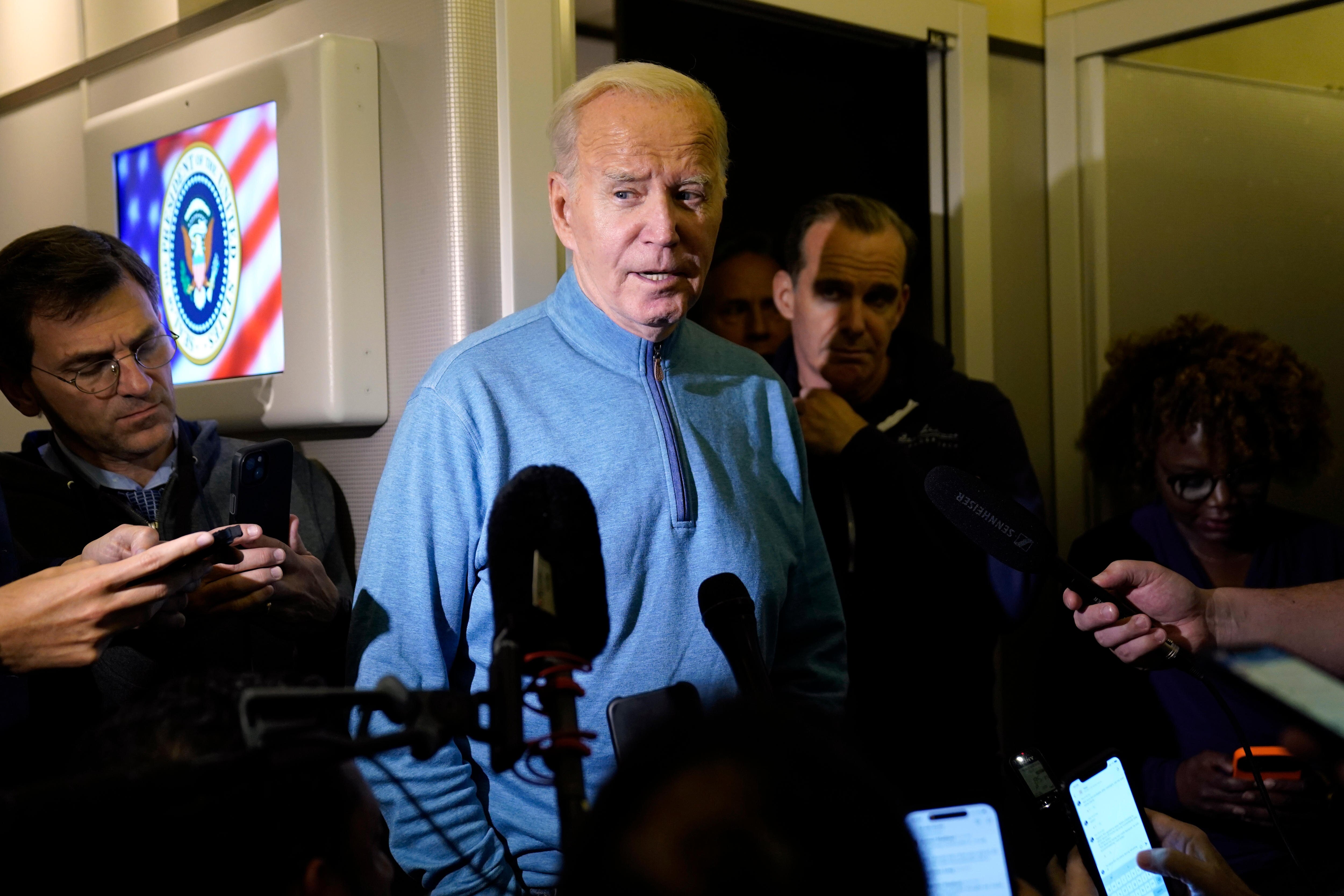 Joe Biden looks on as journalists ask him questions in a corridor