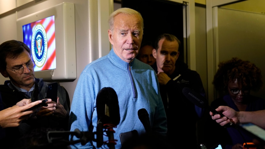Joe Biden looks on as journalists ask him questions in a corridor