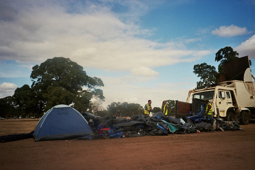 A pile of rubbish and tents next to a rubbish truck.