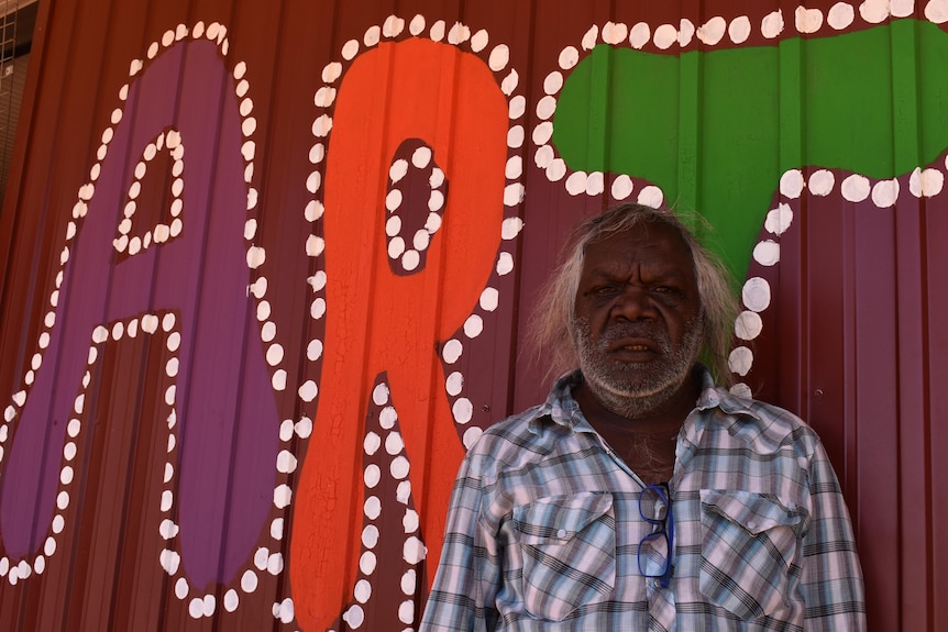 An Aboriginal man standing in front of a colourful painted sign that says 'art'
