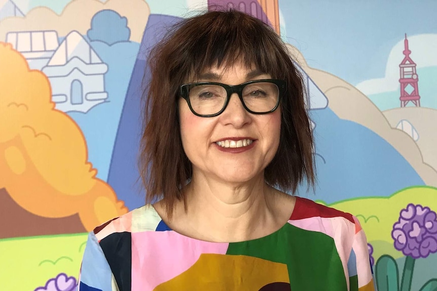 A woman in a multi-coloured shirt standing in front of a cartoon background