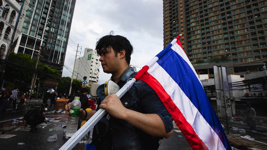 Young man, shown side-on, grim face, flag pole resting on shoulder, street empty and full of empty plastic bottles