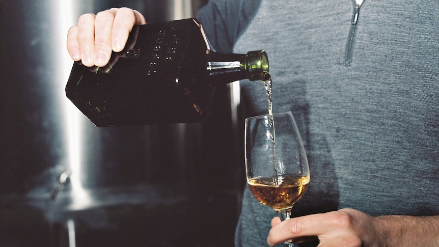 A rye whiskey being poured from a brown square bottle into a rounded clear spirit glass. 