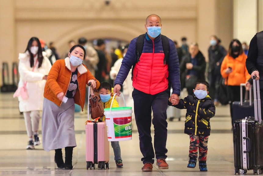 Travellers wearing face masks walk with their luggage at Hankou Railway Station in Wuhan