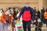 Travellers wearing face masks walk with their luggage at Hankou Railway Station in Wuhan