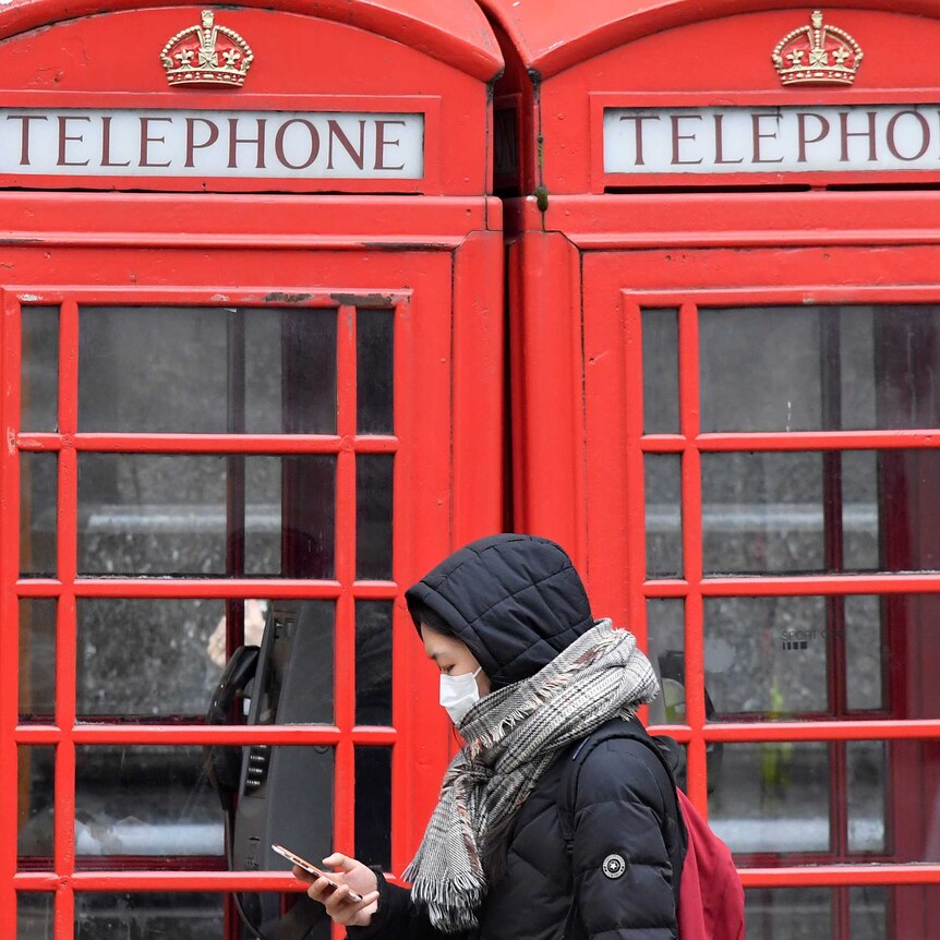 A woman in a face mask walks past London telephone boxes