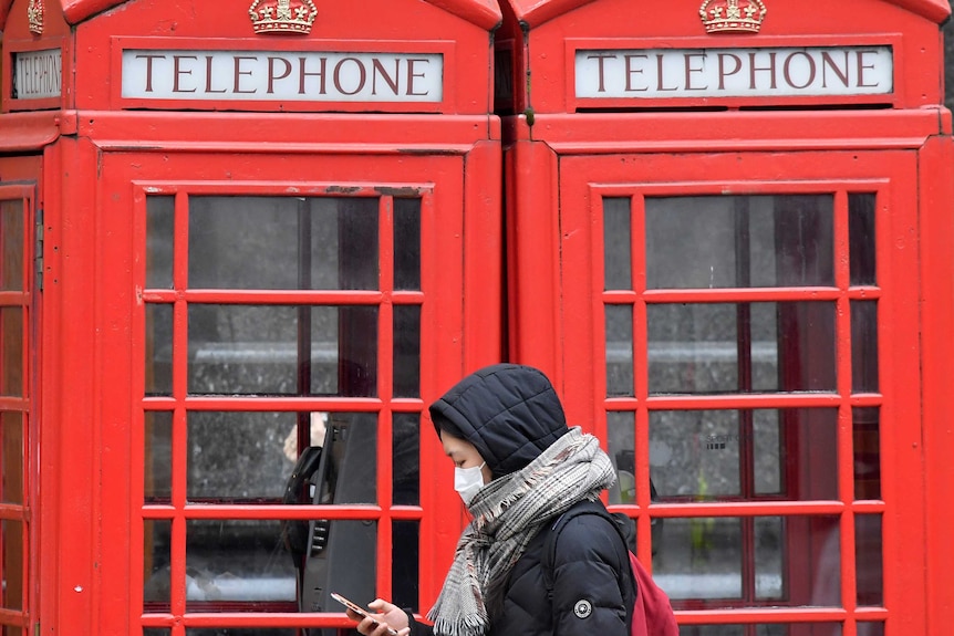 A woman in a face mask walks past London telephone boxes