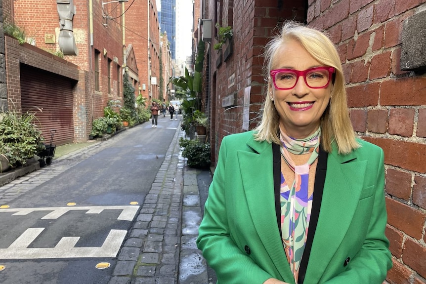 Sally Capp wearing green jacket smiles at the camera while standing in a laneway