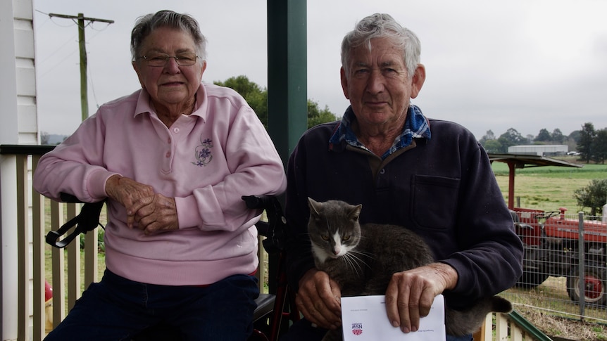 Photo of a man and a woman with a cat sitting and holding a letter.