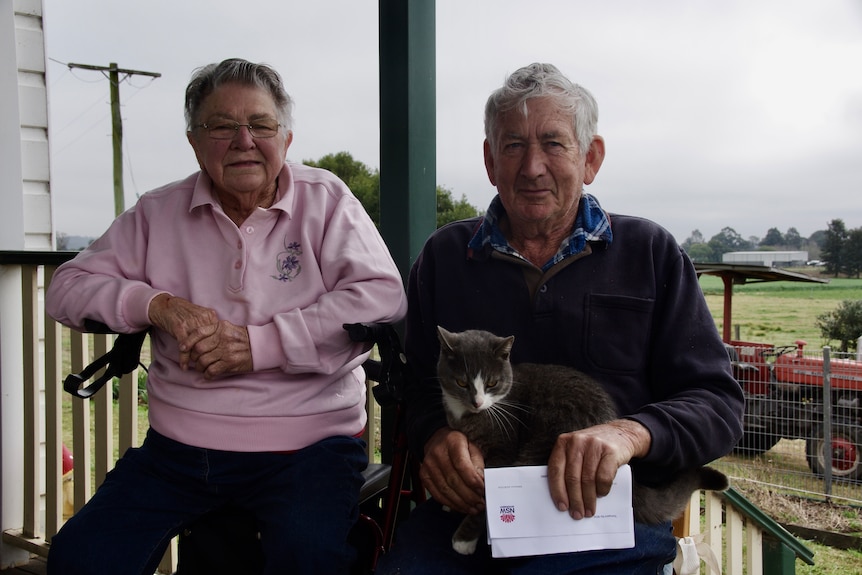 Photo of a man and a woman with a cat sitting and holding a letter.