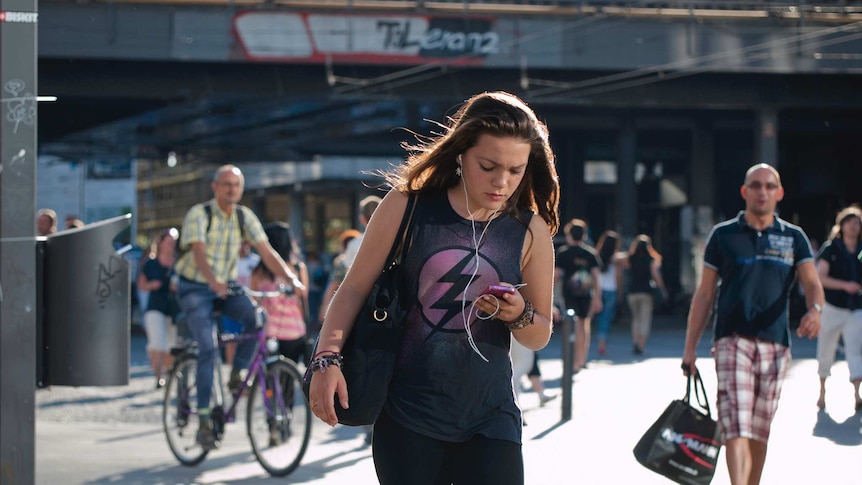 A female pedestrian texts on her phone as she crosses the road.