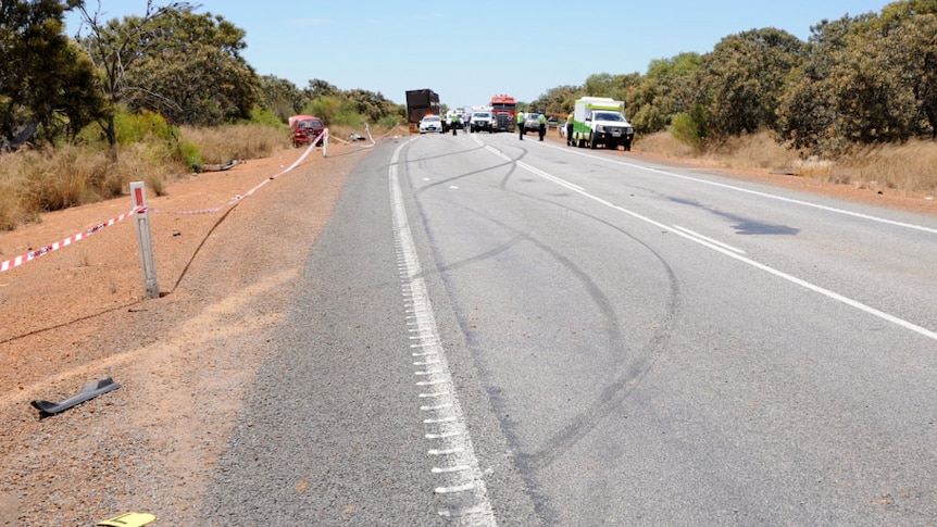 A crash scene on a remote road with police cars and ambulance.