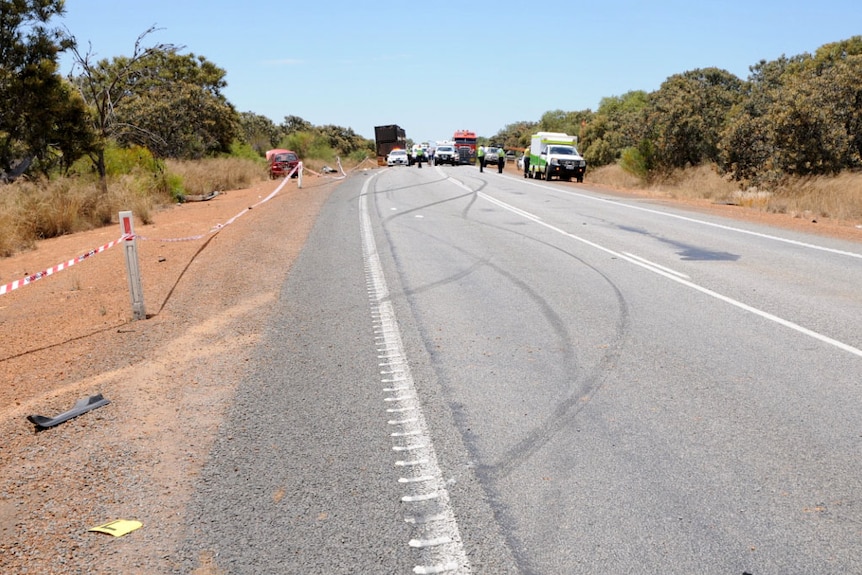 A crash scene on a remote road with police cars and ambulance.