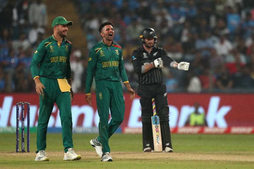 A smiling bowler walks down the pitch after taking a wicket, as a batsman looks down at the non-striker's end.