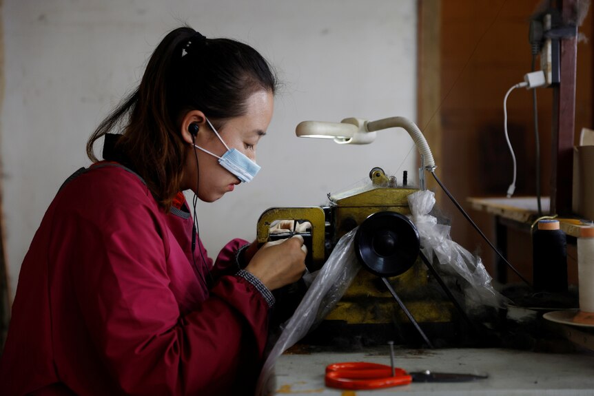 A woman wearing a mask sits at a bench at a mink fur clothing factory in China.