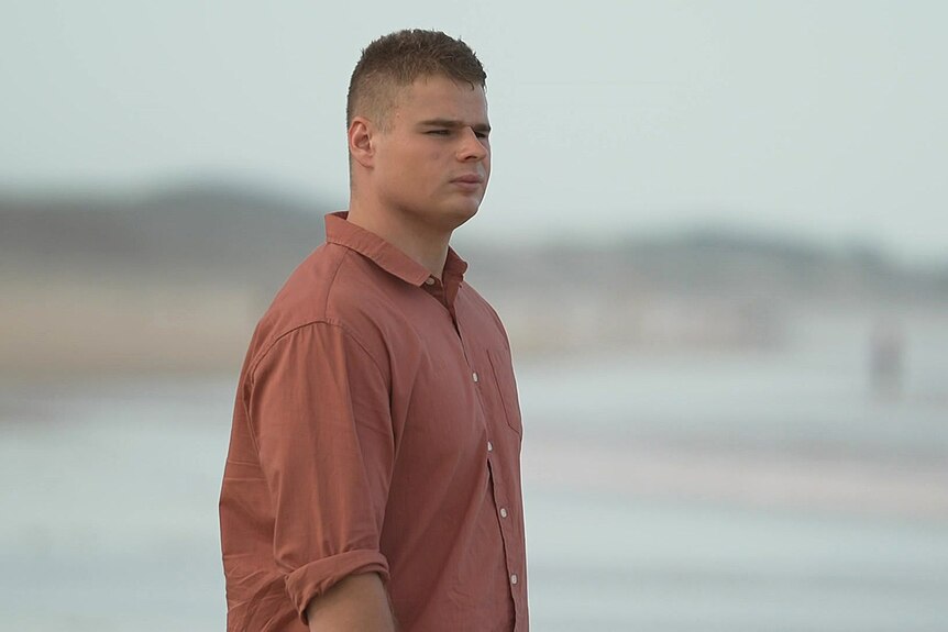 A young man wearing a red collared shirt at the beach.