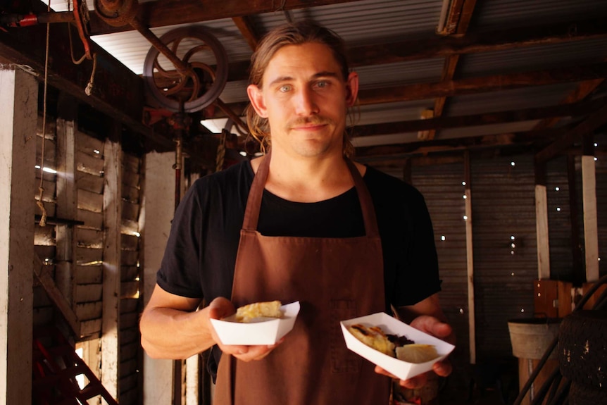 WA chef Paul Iskov holding two "street food"-style meals he has created using native foods.