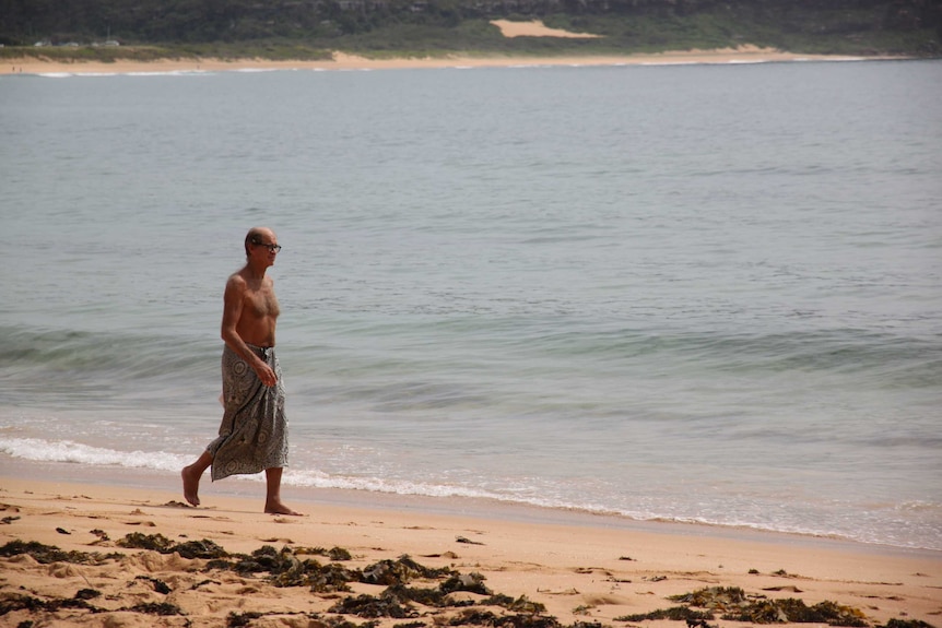 An shirtless man walks along the beach