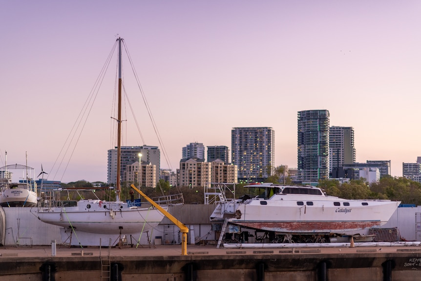 Two boats on a boat ramp with tall buildings in the background during sunset.
